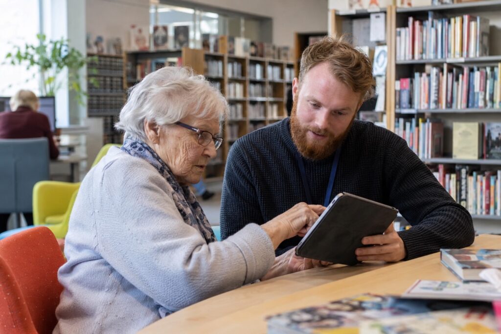 Seniorka ucząca się obsługi tabletu z pomocą bibliotekarza